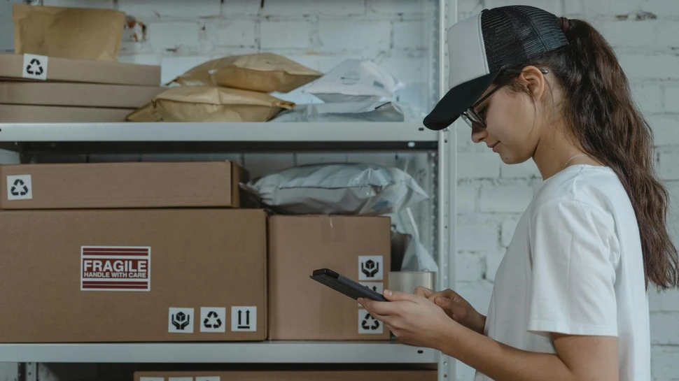 eine Frau steht mit einem Smartphone in einem Lagerraum mit Regal und Kartons