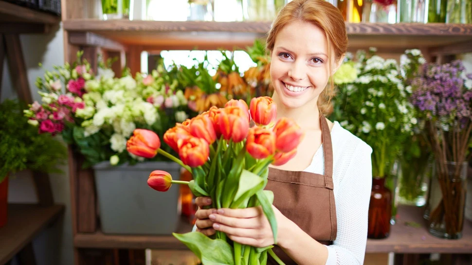 eine Floristin mit brauner Schürze hält einen Strauß mit roten Tulpen in den Händen