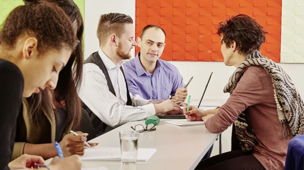 fünf Personen sitzen an einem Tisch und machen sich Notizen