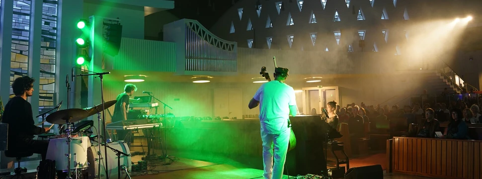 Konzert in einer modernen Kirche mit grüner Beleuchtung und Orgelpfeifen im Hintergrund während der Nacht der Kirchen Hamburg, Musiker auf der Bühne vor Publikum