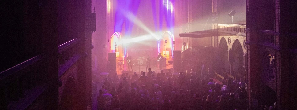 Konzert in einer modernen Kirche mit lilaner Beleuchtung während der Nacht der Kirchen Hamburg, Musiker auf der Bühne vor Publikum