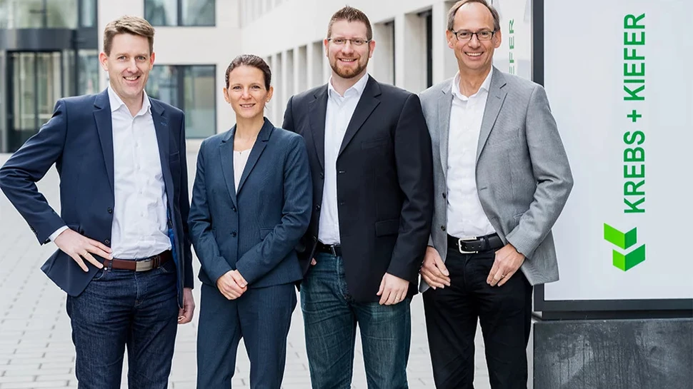 Ein Teil des Teams von KREBS & KIEFER Drei Männer und eine Frau neben einem Schild, auf dem KREBS + KIEFER steht