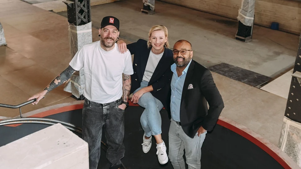 Zwei Männer und eine Frau sitzen auf einem Treppengeländer und schauen nach oben in die Kamera