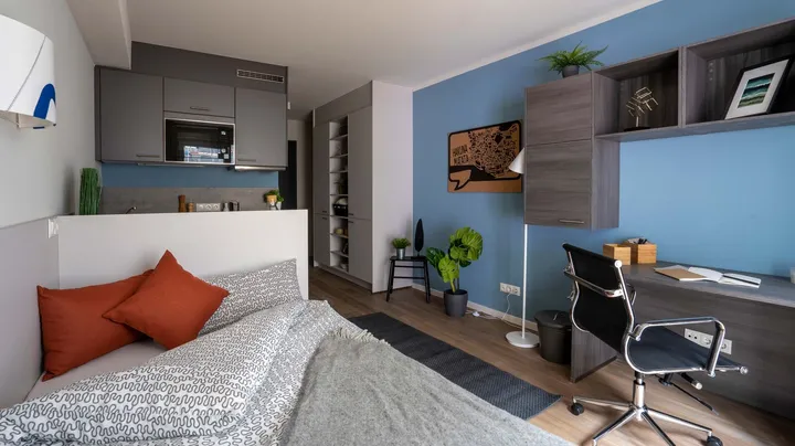 Galerie-Bild 5: blau gestrichenes Zimmer mit Bett, Schreibtisch und kleiner Küchenzeile