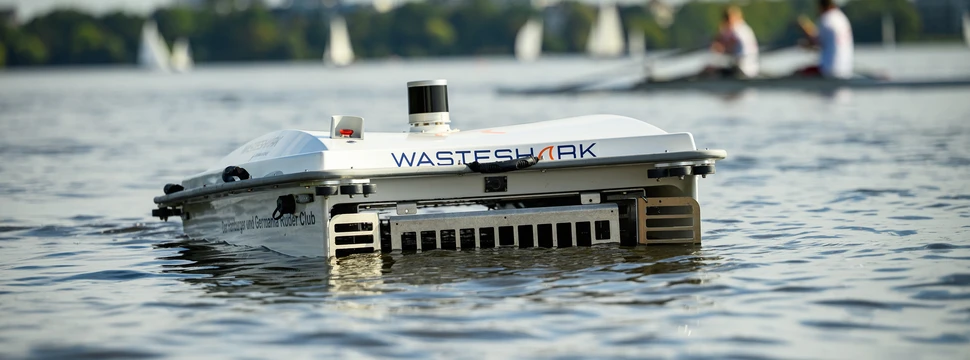WasteShark Der autonome "WasteShark" sammelt Müll auf der Alster, während Ruderer und Segelboote die Sonne genießen – ein Beispiel moderner Umwelttechnologie im urbanen Raum.
