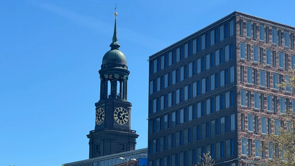 Hamburger Michel Kirchturm hinter Backsteingebäude vor blauem Himmel