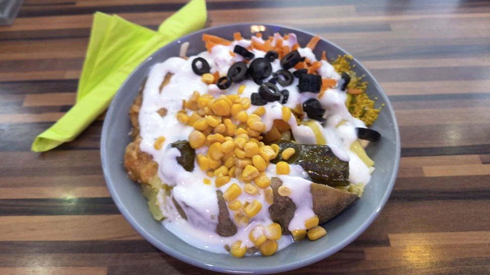 eine Kumpir auf einem grauen Teller gefüllt mit Mais, Oliven, Möhren und Couscous