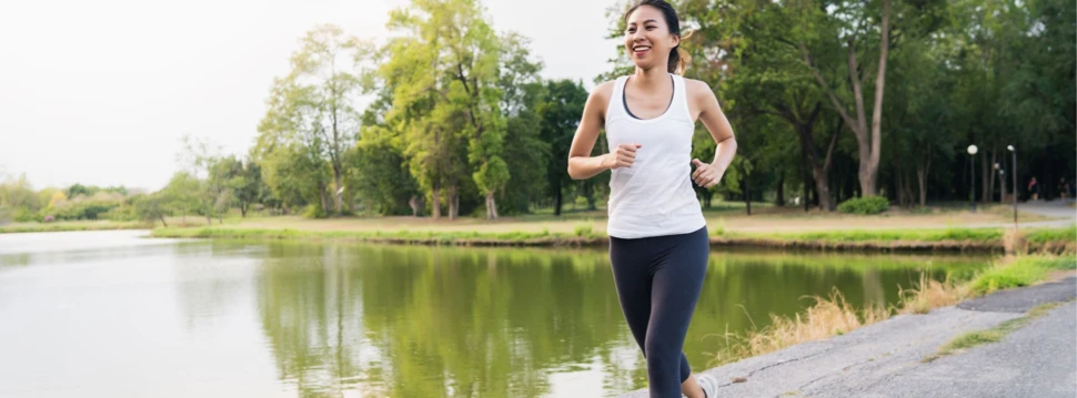 Joggerin läuft am idyllischen Seeufer im Park. Frau joggt bei sonnigem Wetter auf einem Weg am See im grünen Park.