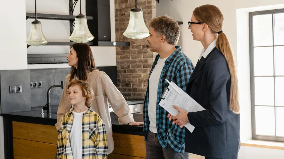 Eine Immobilienmaklerin zeigt einem Paar mit einem Jungen die Küche eines Hauses.