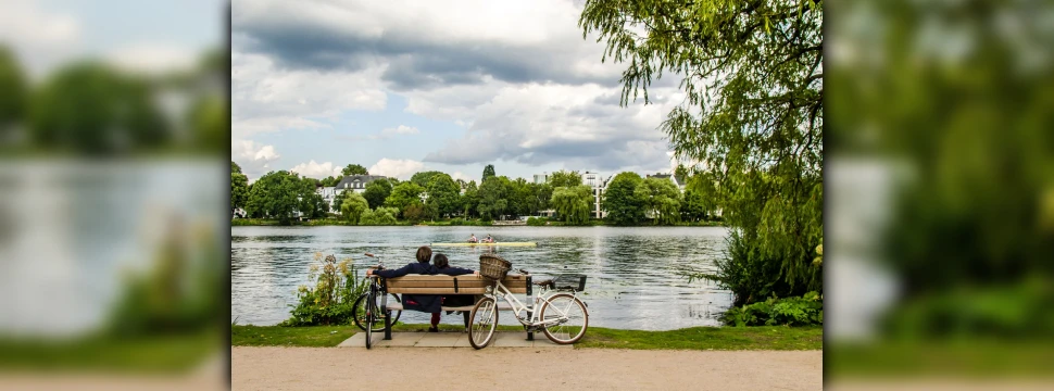 Ein Pärchen sitzt auf einer Parkbank direkt an der Hamburger Alster