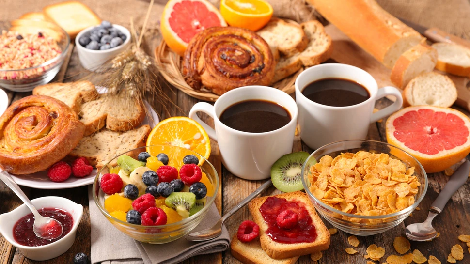 Frühstückstisch mit zwei Tassen Kaffee, Früchten, Cornflakes, Brot und Marmelade