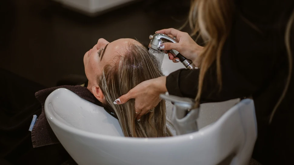Einer blonden Frau werden an einem weißen Waschbecken die Haare gewaschen.