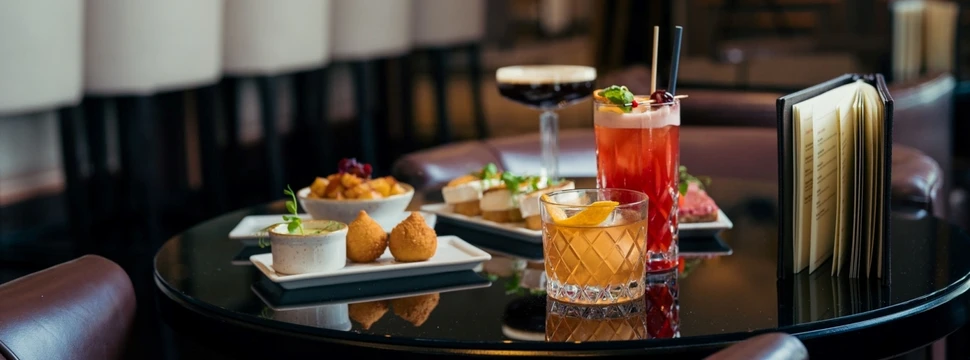 Edle Coctails und kleine Speisen auf einem braunen Tisch in einer Bar