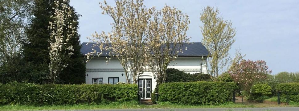 Das Haus Möwe in Steenfeld Ein Haus mit zwei Ferienwohnungen darin in Schleswig-Holstein mit einer Hecke im Vordergrund und Bäumen im Hintergrund