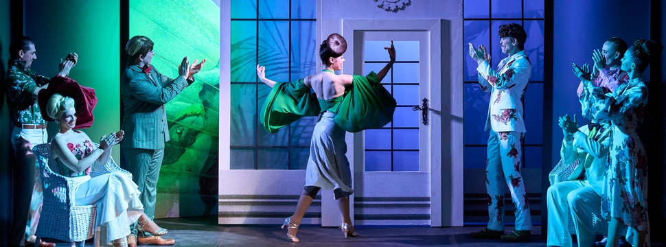 Theaterszene aus "Die lustige Witwe" mit Darstellern in historischen Kostümen auf bunter Bühne