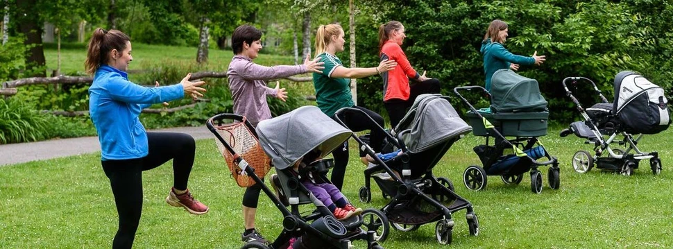 Frauen mit Kinderwagen machen Sport auf einer Wiese