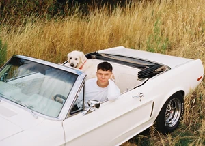 Mann sitzt mit einem Hund in einem weißem Caprio