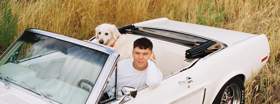 Mann sitzt mit einem Hund in einem weißem Caprio