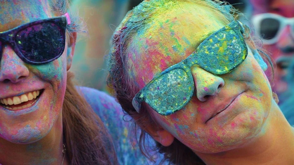 zwei Frauen mit Sonnenbrillen, die beim Holi Festival bunte Farben abbekommen haben