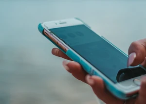 Ein Handy in der Hand von einem Menschen mit Wasser im Hintergrund