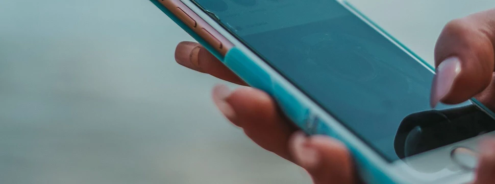 Ein Handy in der Hand von einem Menschen mit Wasser im Hintergrund