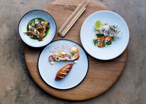 Drei Teller mit fein angerichtetem Essen auf einem runden Holzbrett