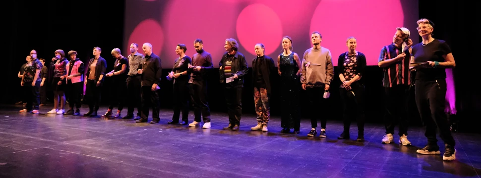 Mehrere Menschen in einer Reihe auf einer Bühne mit pinkem Bühnenbild