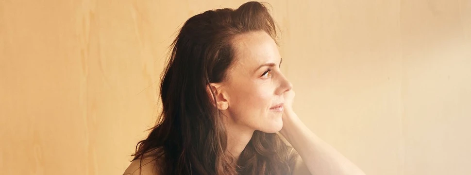 Anna Depenbusch in beigem Outfit sitzt nachdenklich vor hellem Hintergrund.