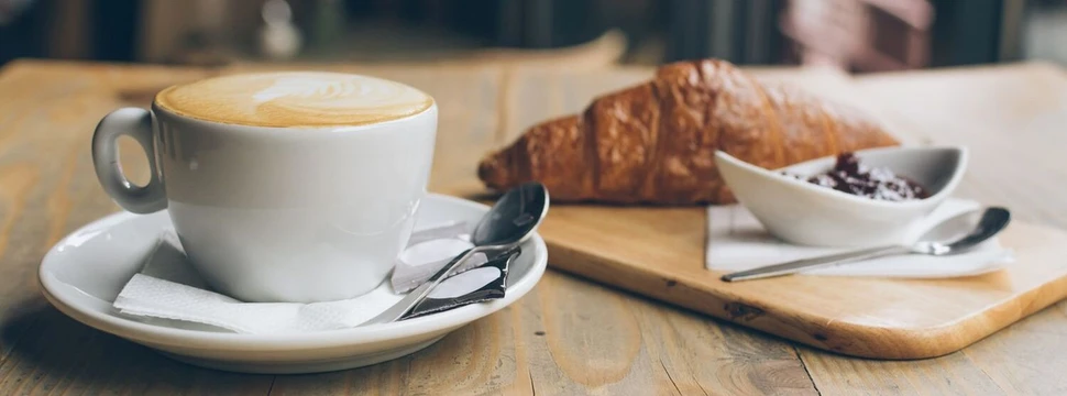 Croissant und Café au Lait in einem französischen Café Weiße Tasse mit Milchkaffee und ein Croissant auf einem Brettchen