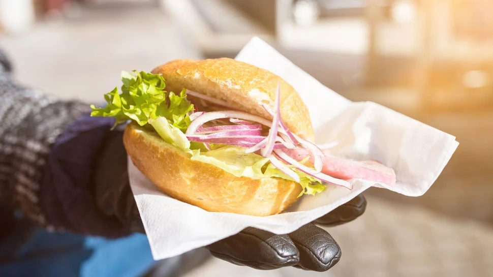 eine Hand mit schwarzem Handschuh hält ein Fischbrötchen