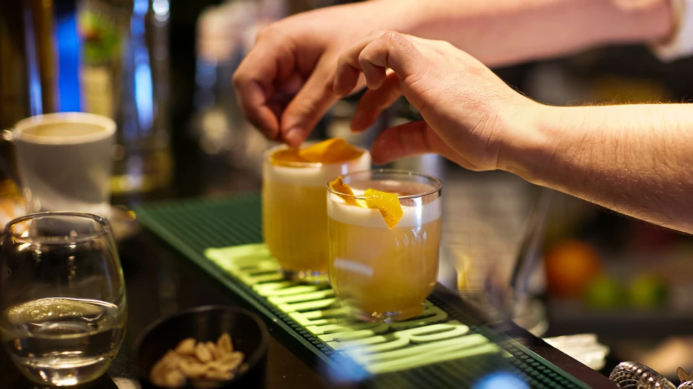 Barkeeper stellt 2 Cocktails auf den Tresen der Bar und garniert einen davon mit Zitronenzeste