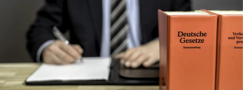 Zwei Gesetzbücher, dahinter eine Person, die einen Antrag unterzeichnet