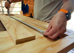 Handwerker misst präzise Maße auf einer Holzplatte in der Werkstatt.