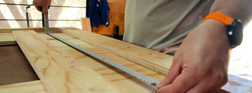 Handwerker misst präzise Maße auf einer Holzplatte in der Werkstatt.
