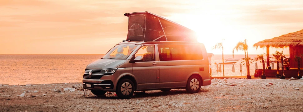 Camper mit geöffneter Seitentür steht am Meer