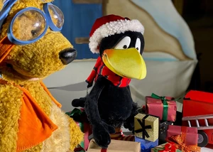 Der kleine Rabe Socke mit einer Weihnachtsmütze auf dem Kopf sitzt hinter einem kleinen Geschenkeberg