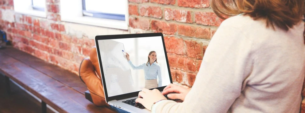 Eine Frau sitzt mit hochgelegten Beinen neben einer Backsteinwand und hat einen aufgeklappten Laptop auf den Beinen.