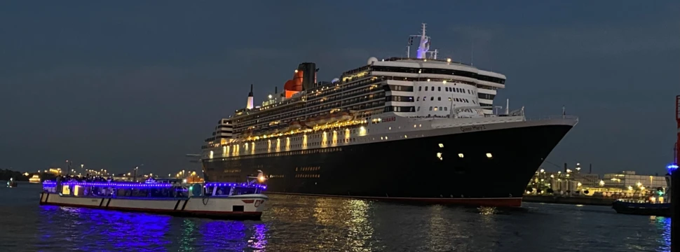 Queen Mary 2 Kreuzfahrtschiff bei Dämmerung im Hafen mit blau beleuchtetem Boot im Vordergrund