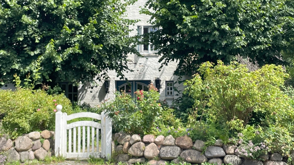 Reetdachhaus mit Bäumen und weißer Gartenpforte