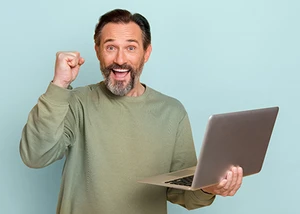 Ein jubelnder und lächelnder Mann hält einen aufgeklappten Laptop in der linken Hand