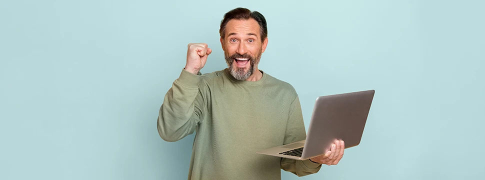 Ein jubelnder und lächelnder Mann hält einen aufgeklappten Laptop in der linken Hand