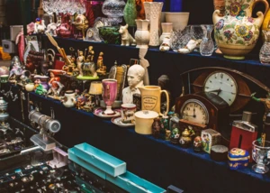 Antiquitätenstand mit Porzellan, Uhren, Schmuck und Sammlerobjekten auf dunklen Verkaufstischen.
