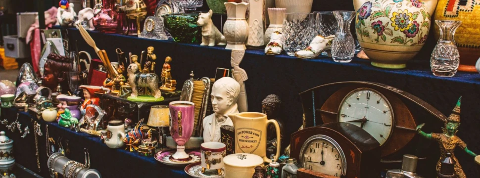 Antiquitätenstand mit Porzellan, Uhren, Schmuck und Sammlerobjekten auf dunklen Verkaufstischen.