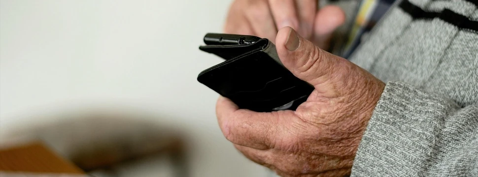 Ein Senior hält ein schwarzes Smartphone in der Hand