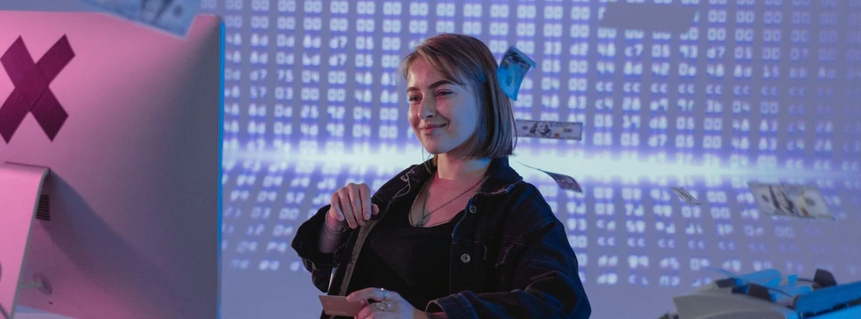 Junge Frau mit Kurzhaarschnitt sitzt lächelnd am Computer und hält eine Kreditkarte in der Hand.
