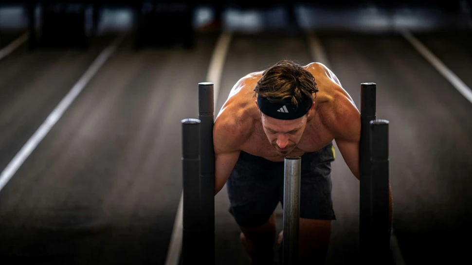 ein Mann mit freiem Oberkörper schiebt einen Gewichtsschlitten beim HYROX Training