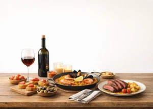 Ein Holztisch mit Tapas, Paella, Fleisch und einem Rotwein-Glas samt Flasche