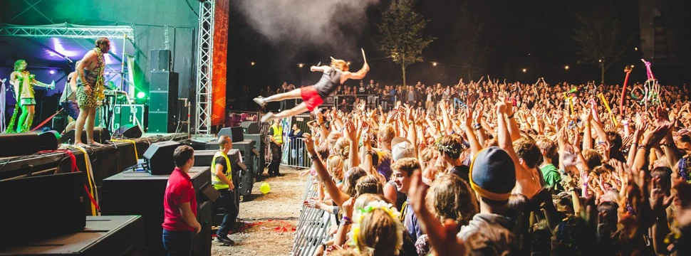 Sänger springt von beleuchteter Festivalbühne in eine jubelnde Menschenmenge mit erhobenen Händen bei Nacht.