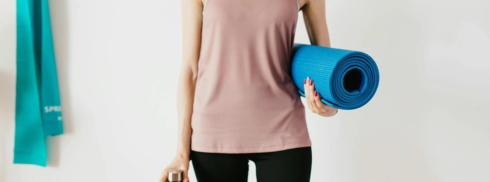 Workout Frau mit Yogamatte unter dem Arm und Flasche in der Hand