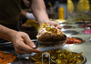 Eine Kumpir wird mit frischen Zutaten belegt